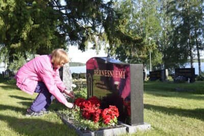 Irma Siirtola laski emäntä Hilma Mustikkamaan haudalle valkoisen neilikan. Sukuhautaan haudatun Mustikkamaan muistolaatta on punaisten begonioiden takana.