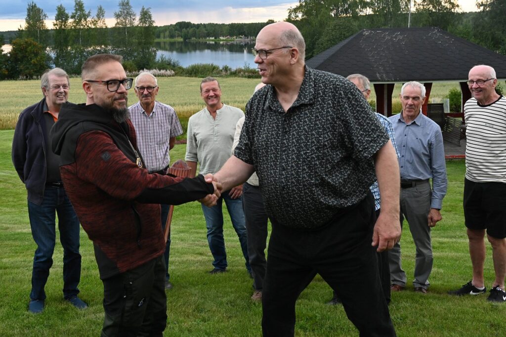 Leijonat seuraavat, kuinka Lions Club Vimpelin puheenjohtajuus siirtyy virallisen kädenpuristuksen myötä Tuomas Mäkelältä (edessä oik.) Hannu Takalalle. Kuva: Toimitus.