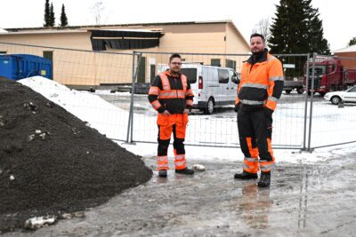 Jarmo Arpala ja Seppo Hernesniemi hiekoitussepelikasan edessä Hippopuiston edustalla. Taustalla valmistuu uusi kirjastorakennus, joka miesten mukaan etenee aikataulussa.